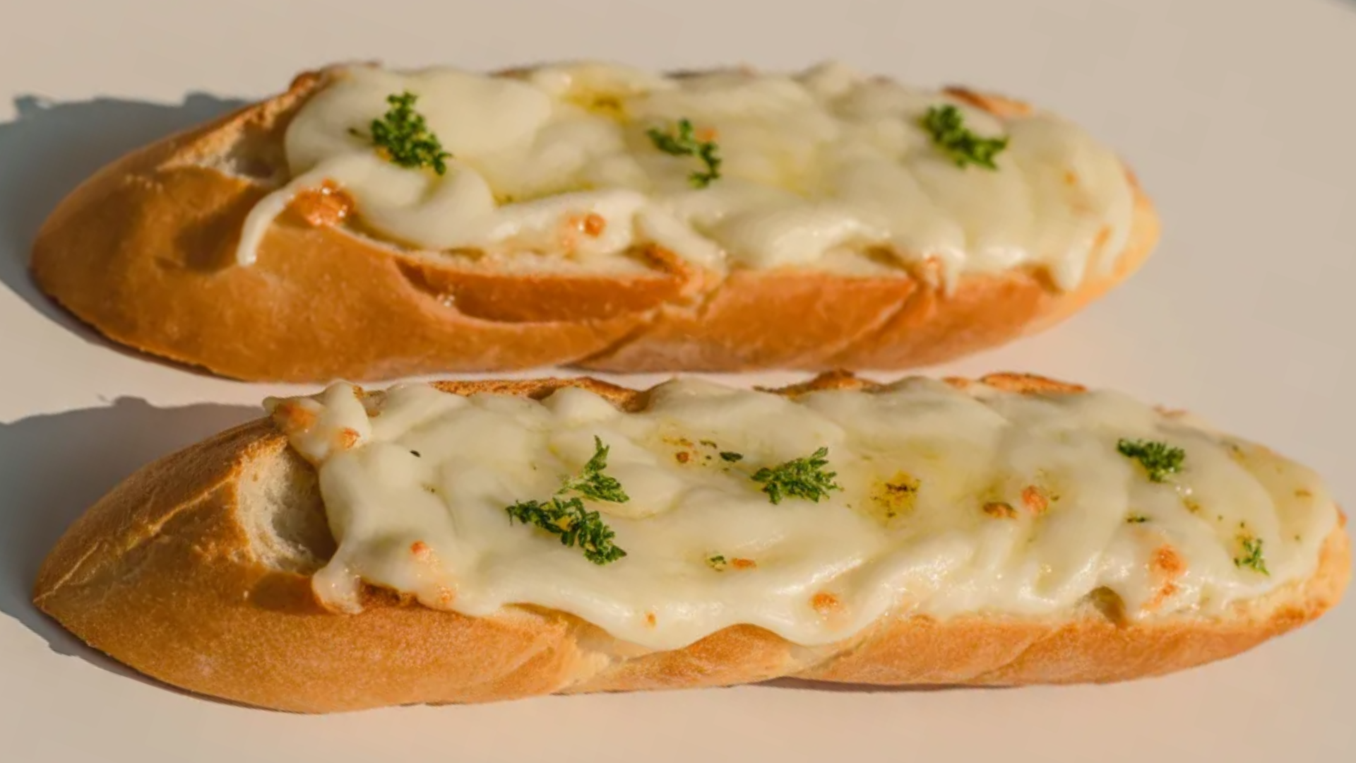 Simple cheesy garlic bread on a white table with melted mozzarella and garlic butter