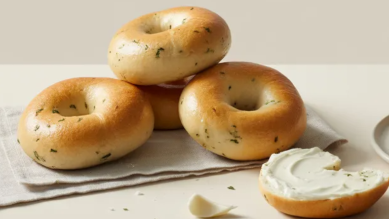 Garlic herb bagels on a white plate with cream cheese on a clean white table and soft even lighting