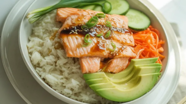 Salmon rice bowl with fluffy white rice, pan-seared salmon, avocado slices, cucumber, carrots, and sesame seeds served on a white plate with natural light