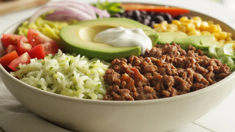 A realistic overhead photo of a homemade beef burrito bowl filled with seasoned ground beef, rice, beans, corn, avocado, cheese, and fresh vegetables in a white bowl on a bright white table.