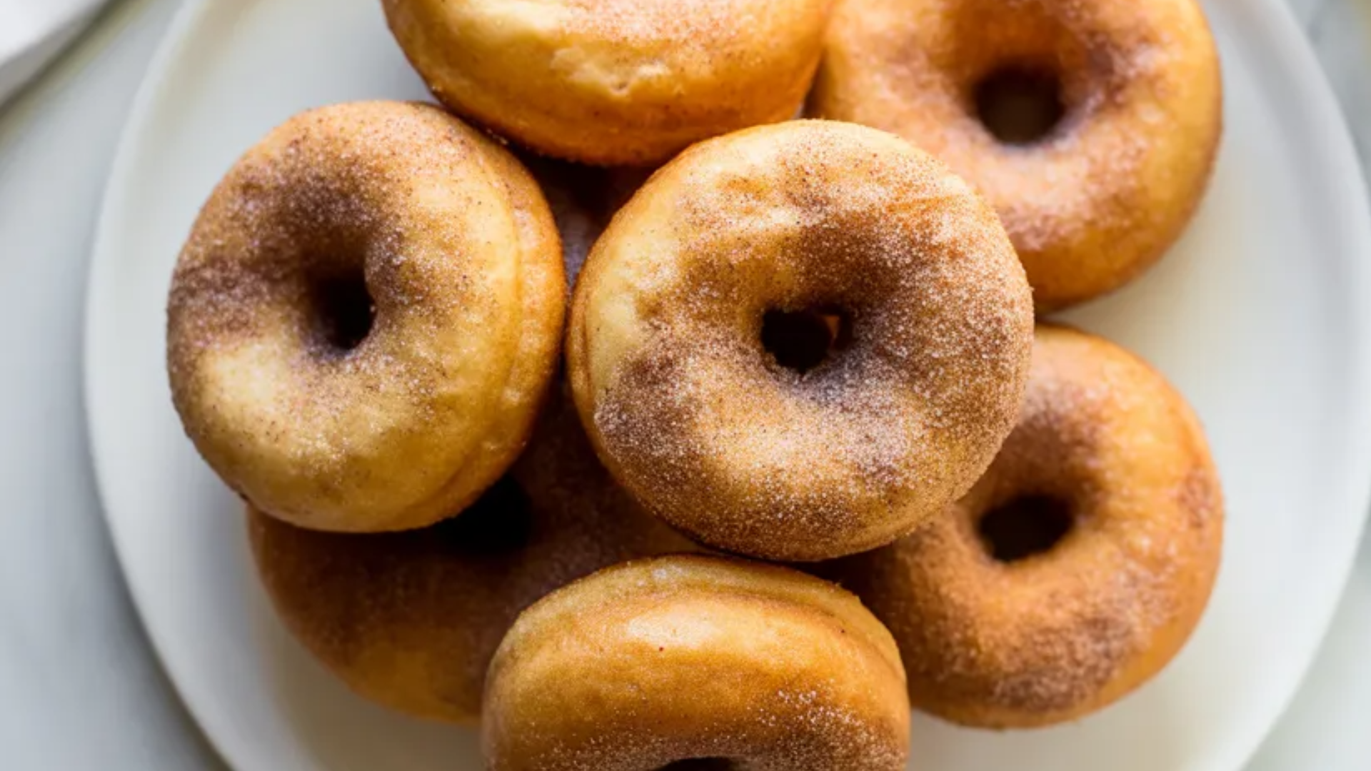 Soft and fluffy air fryer donuts coated in cinnamon sugar served on a white plate with a clean white background