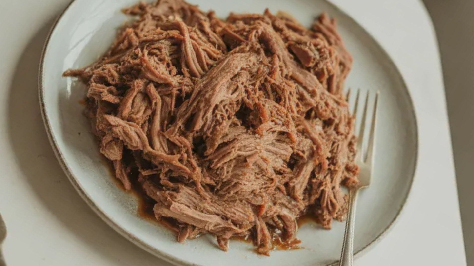 Slow cooker shredded beef served on a white plate with juicy tender texture