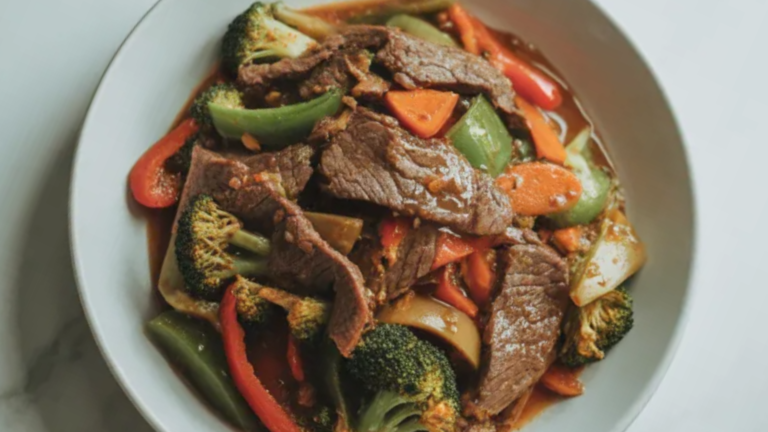 Close-up of healthy beef stir fry with tender beef strips, broccoli, bell peppers, and carrots in a light sauce served in a white bowl on a clean white table