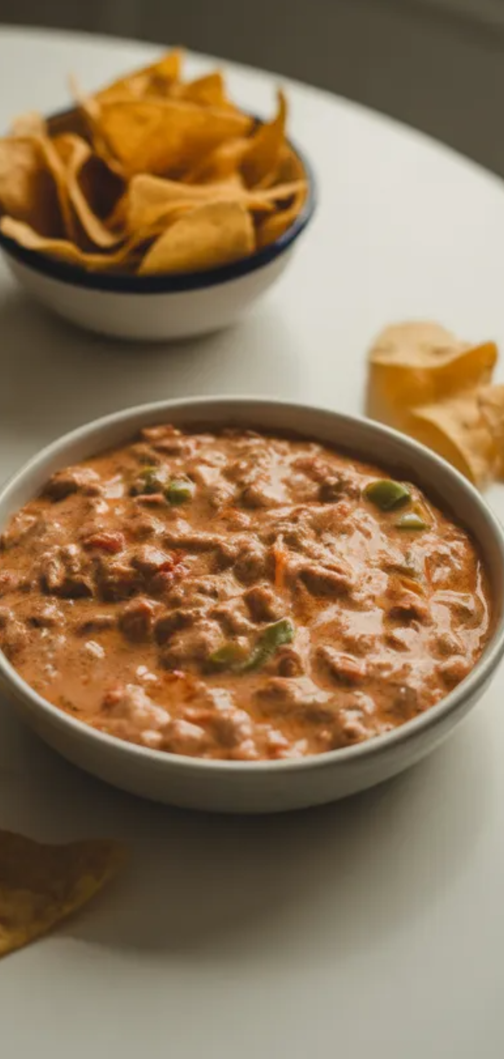 Warm melted cheese Rotel dip in a minimal white setting with crispy chips on the side