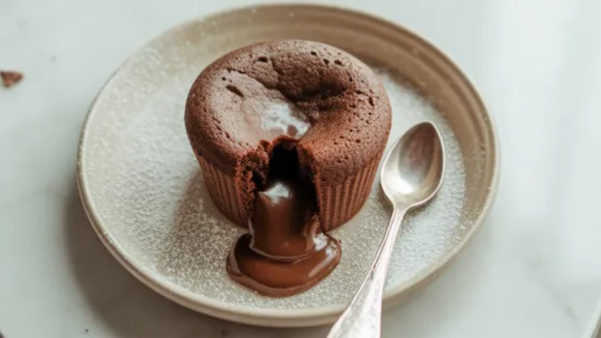 A realistic air fryer lava cake in a white ramekin with melted chocolate flowing from the center on a bright white table